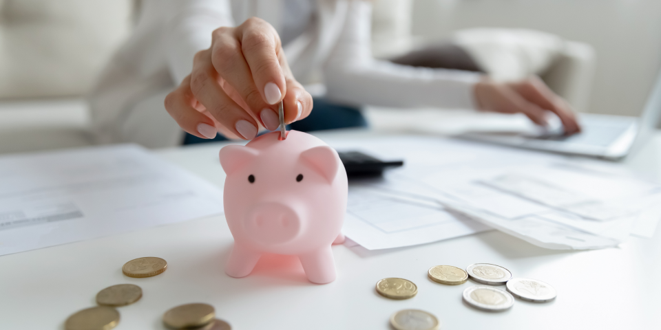 Person typing on laptop putting money into piggy bank