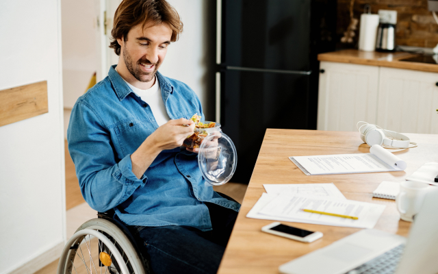 Man in wheelchair at kitchen table eating