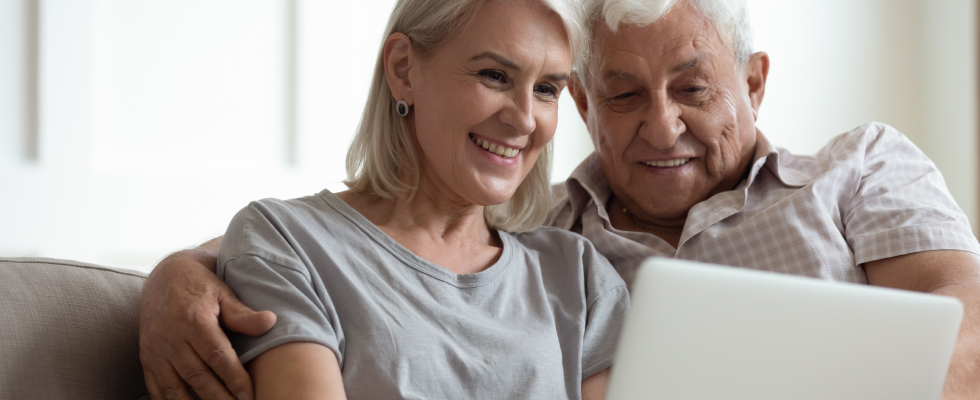 Elderly couple sitting down, looking at laptop